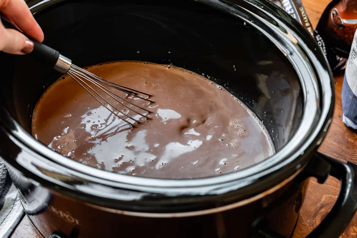 a whisk stirring hot chocolate in a black slow cooker.