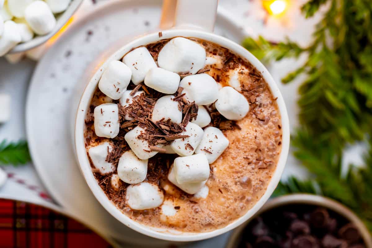 overhead shot of hot chocolate in a mug with mini marshmallows and chopped chocolate, with twinkle lights.