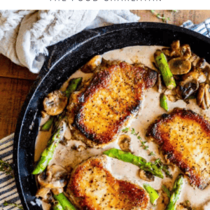 A cast iron skillet with pork chops in sauce, golden-brown and pan-seared, surrounded by asparagus and mushrooms. A beige kitchen towel rests nearby on a wooden table. Text reads: 30 Minute Pan-Seared Pork Chops.