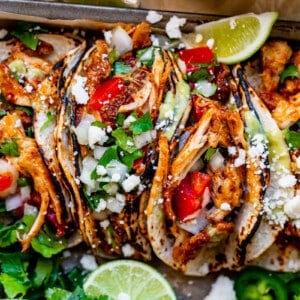 four tacos side by side with juicy chicken, tomato, onion, cilantro, and lime.