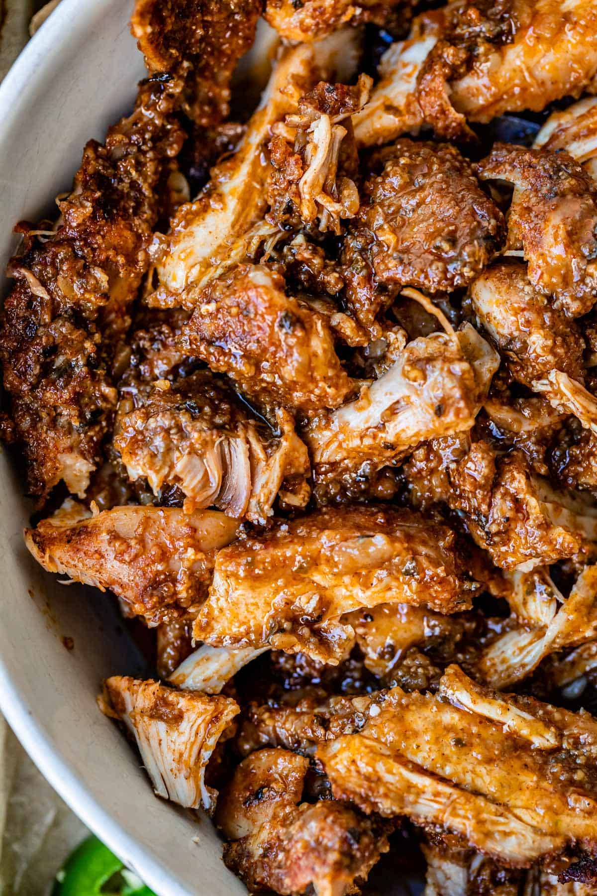 super close up picture of cooked, shredded chicken with tons of seasoning in a white bowl.