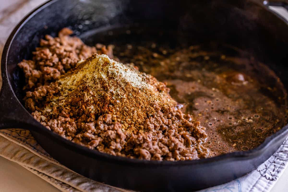 adding taco seasoning to ground beef in a cast iron skillet.