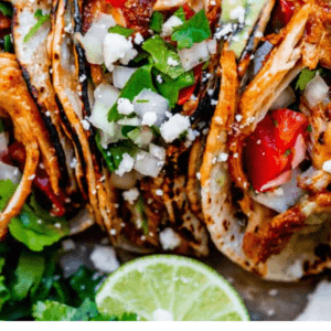 Shredded Chicken tacos on a tray with tomatoes, onions, cilantro, and cheese.