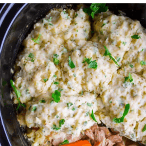 Overhead view of Crockpot Chicken and Dumplings in a slow cooker, featuring shredded chicken, carrots, and fluffy dumplings topped with chopped parsley. Text reads: Ultimate comfort food. Chicken & dumplings. Slow cooker recipe.