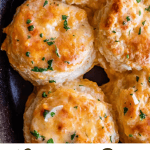 Golden, cheesy cheddar bay biscuits topped with chopped parsley are shown close together in a skillet. Text reads “Cheddar Bay Biscuits (Red Lobster Copycat)” and “The Food Charlatan.”.