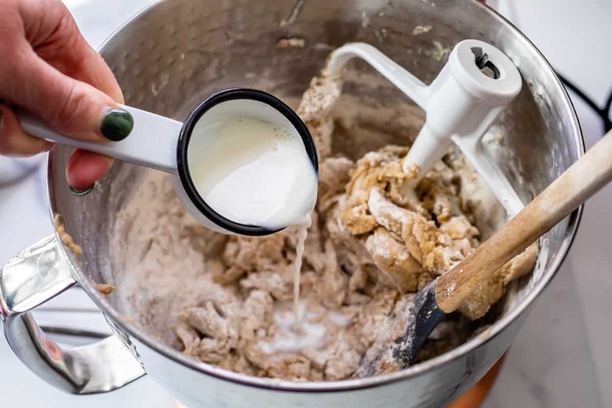 adding milk to frosting in a stand mixer bowl.