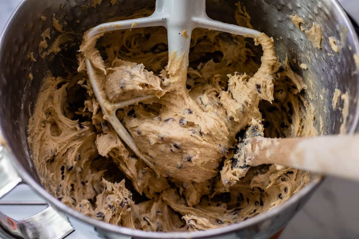 cookie dough frosting on a paddle attachment for a stand mixer bowl with a spoon.