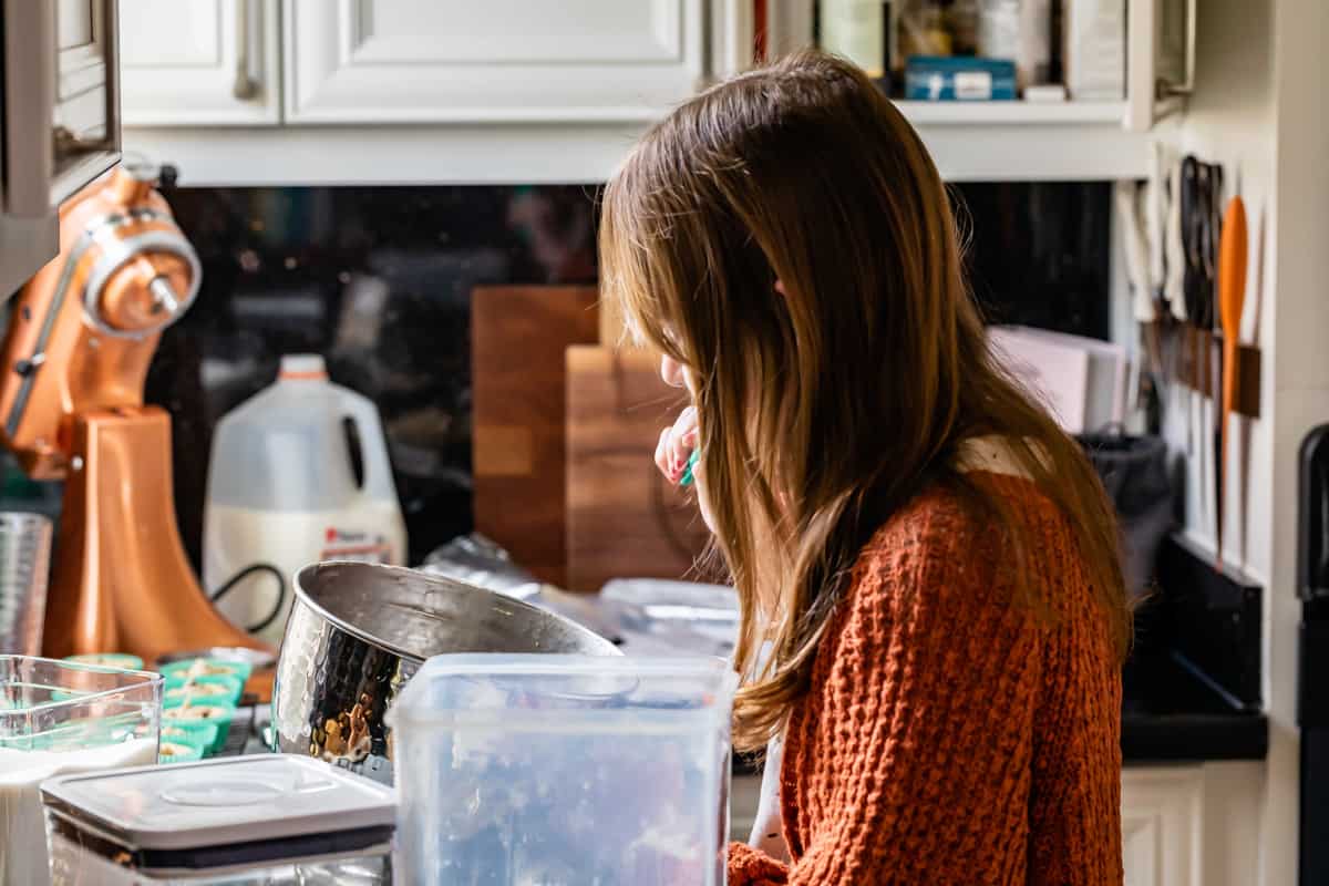 a girl eating cookie dough frosting in a kitchen.