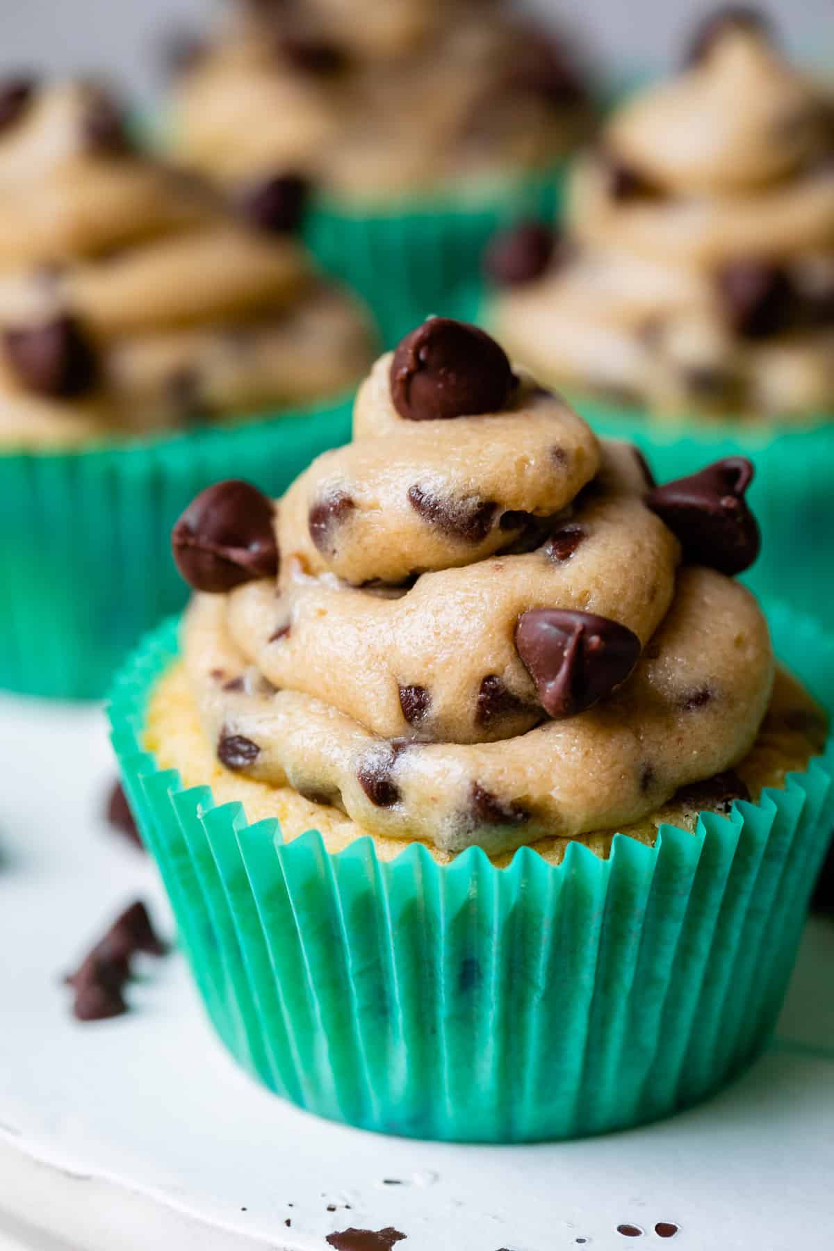 cookie dough frosting piped on top of cupcakes in green liners.