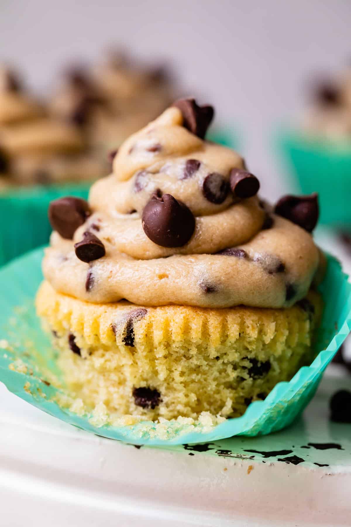 cupcake partially removed from its wrapper with chocolate chips and cookie dough frosting.