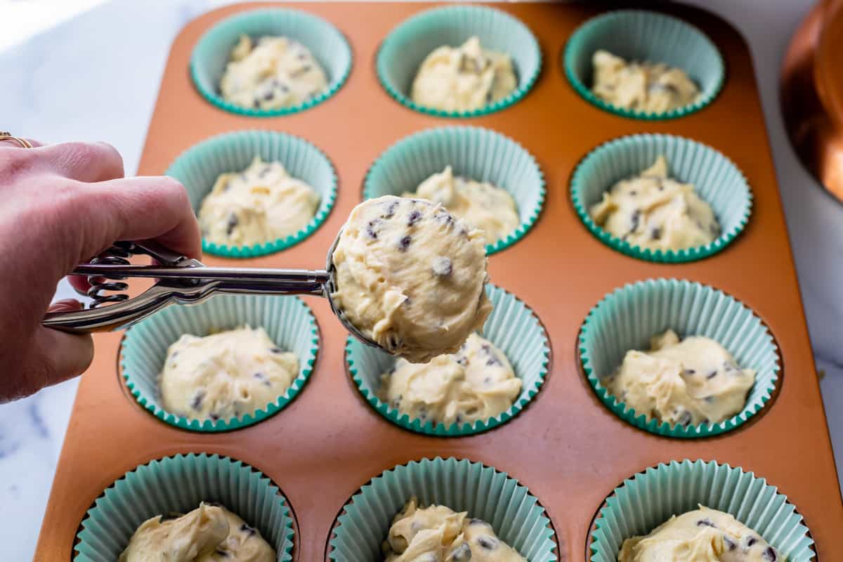 using a cookie scoop to put cupcake batter into cupcake liners in a muffin tin.