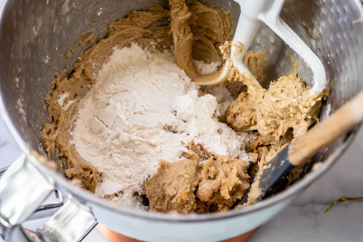 adding flour to cookie dough frosting in a stand mixer bowl.