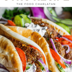 Two Greek gyros filled with meat, tomatoes, cucumbers, red onions, and creamy tzatziki sauce are wrapped in soft pita bread. The image is vibrant and appetizing, with “Greek Gyro” text at the top.