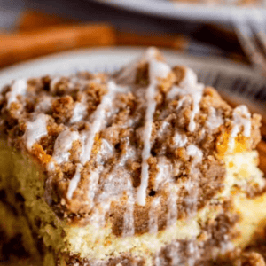 A close-up of a slice of sour cream coffee cake topped with crumbly streusel and vanilla glaze, served on a patterned plate. Text above reads “Homemade Coffee Cake with Vanilla Drizzle.”.