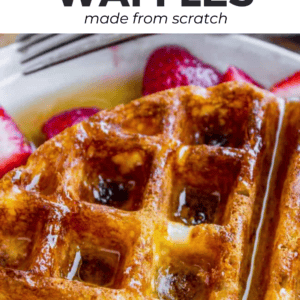 Close-up of a golden brown waffle topped with syrup, served with sliced strawberries. Text at the top reads “Homemade Waffles made from scratch” with “waffle recipe” featured, and at the bottom, “the Food Charlatan.”.