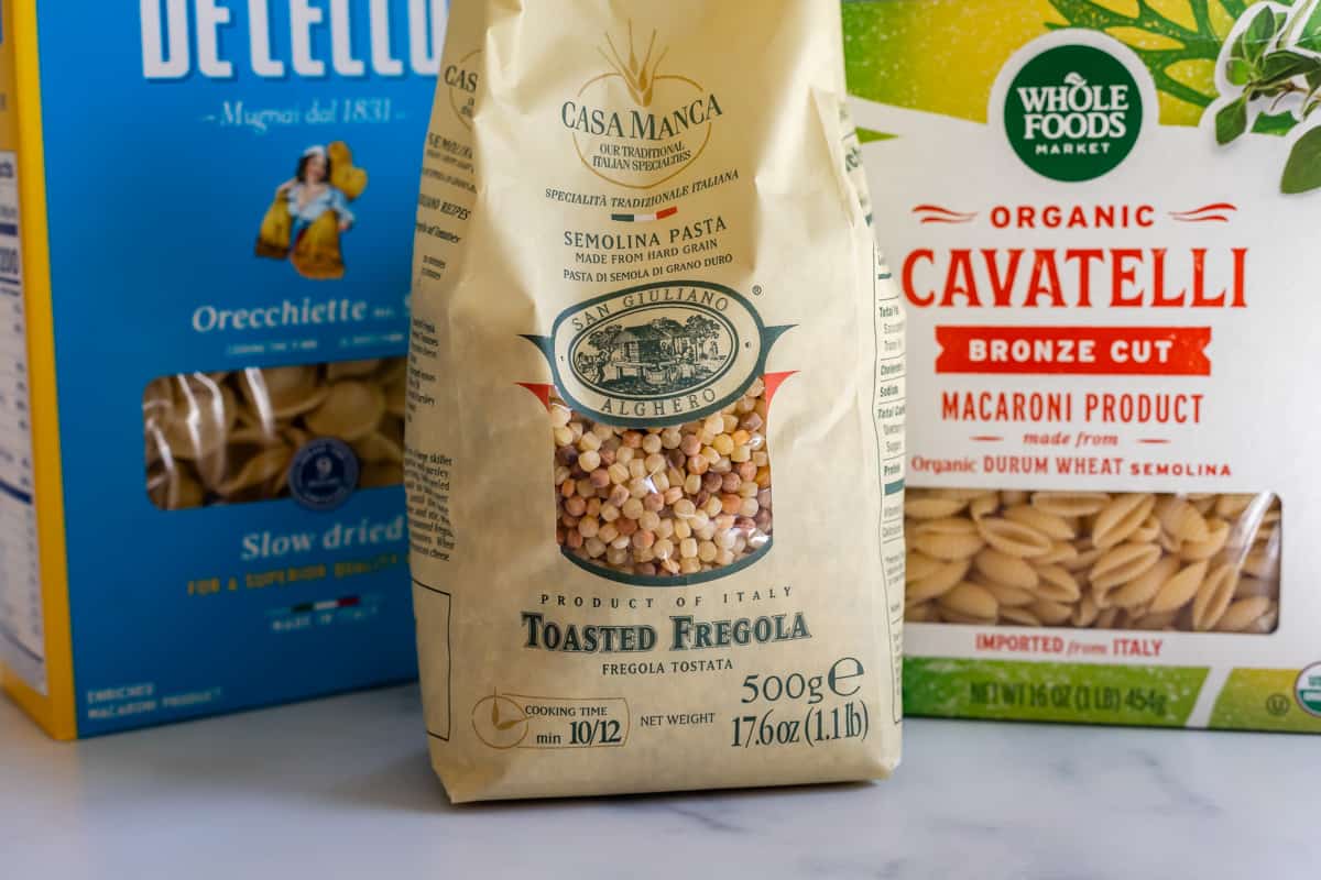 three different types of pasta; fregola, cavatelli, and orecchiette in packaging on a counter. 