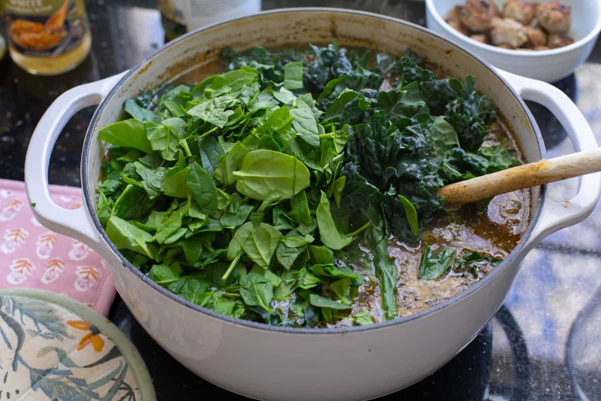 stock pot filled with broth with a large pile of spinach and kale.