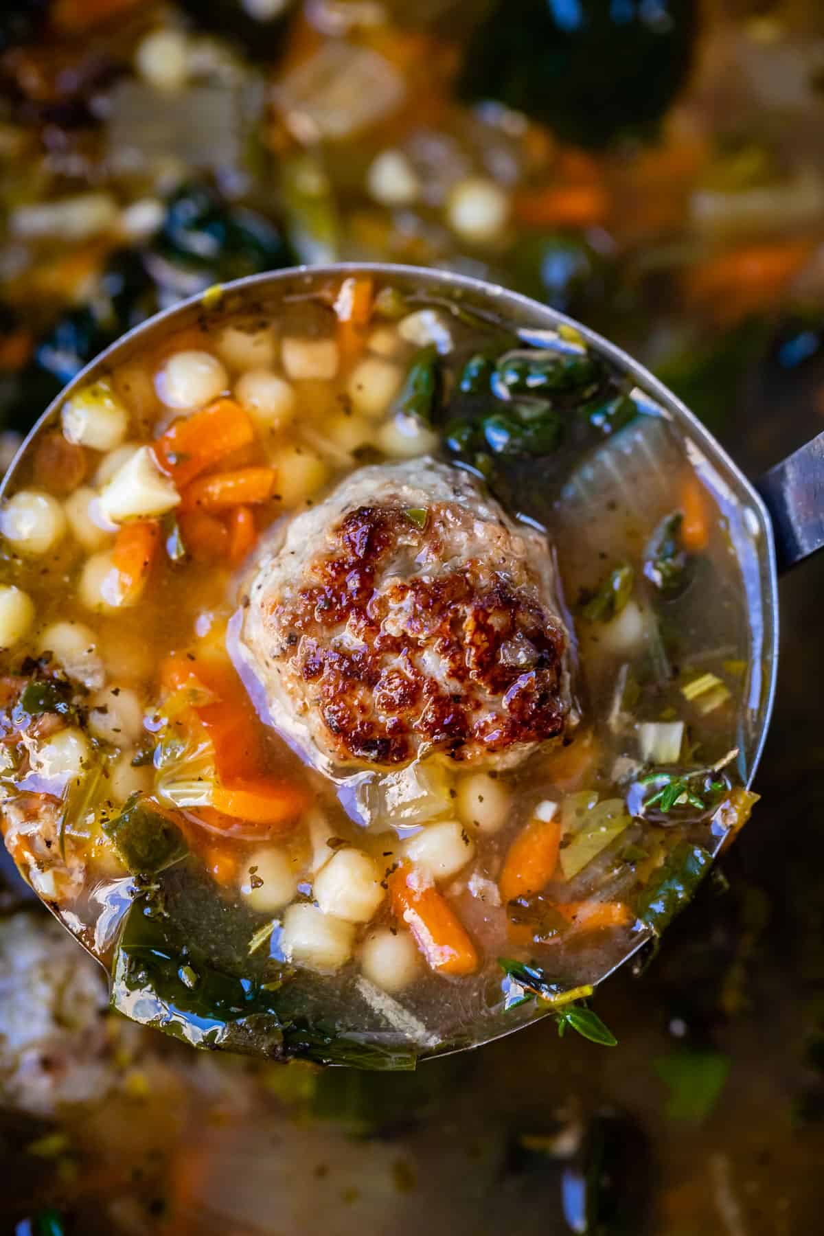 metal ladle filled with italian wedding soup which has a meatball, broth, pasta, and vegetables.