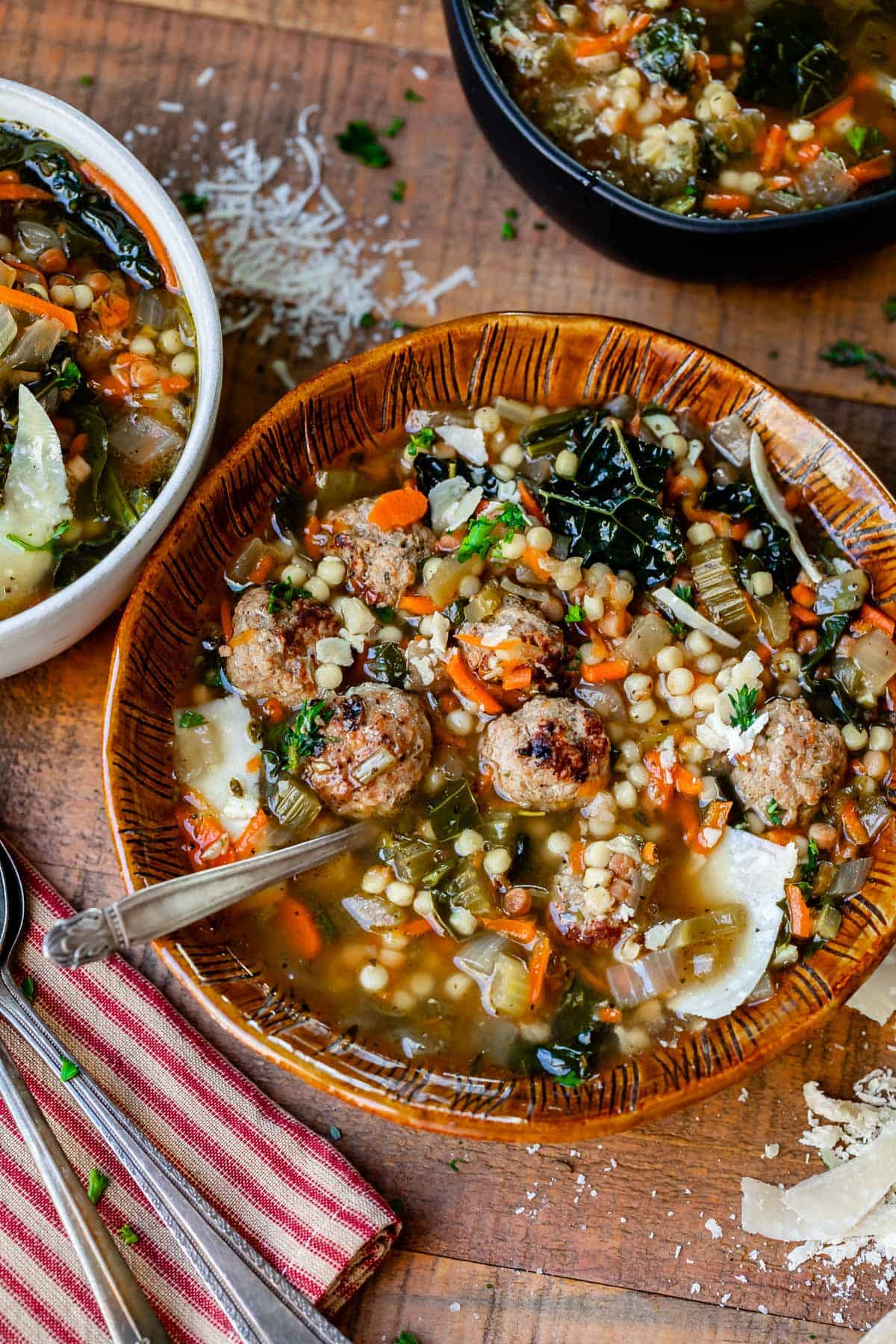 ceramic bowl on cutting board filled with italian wedding soup of greens, meatballs, pasta, and broth.