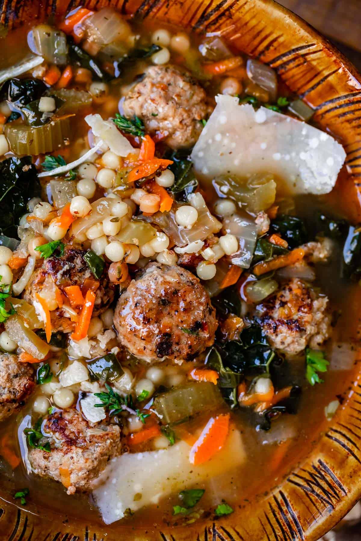 close up of easy italian wedding soup with meatballs, pasta, greens, and broth in a brown clay bowl.