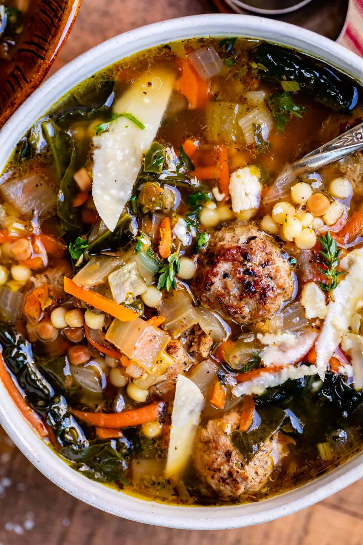 close up of italian wedding soup with deep broth, meatballs, pasta and greens in a white bowl.