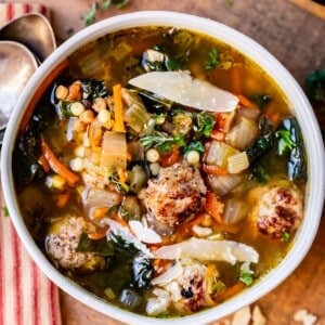 Italian Wedding Soup made of broth, meatballs, greens, and pasta in a white bowl on a cutting board.