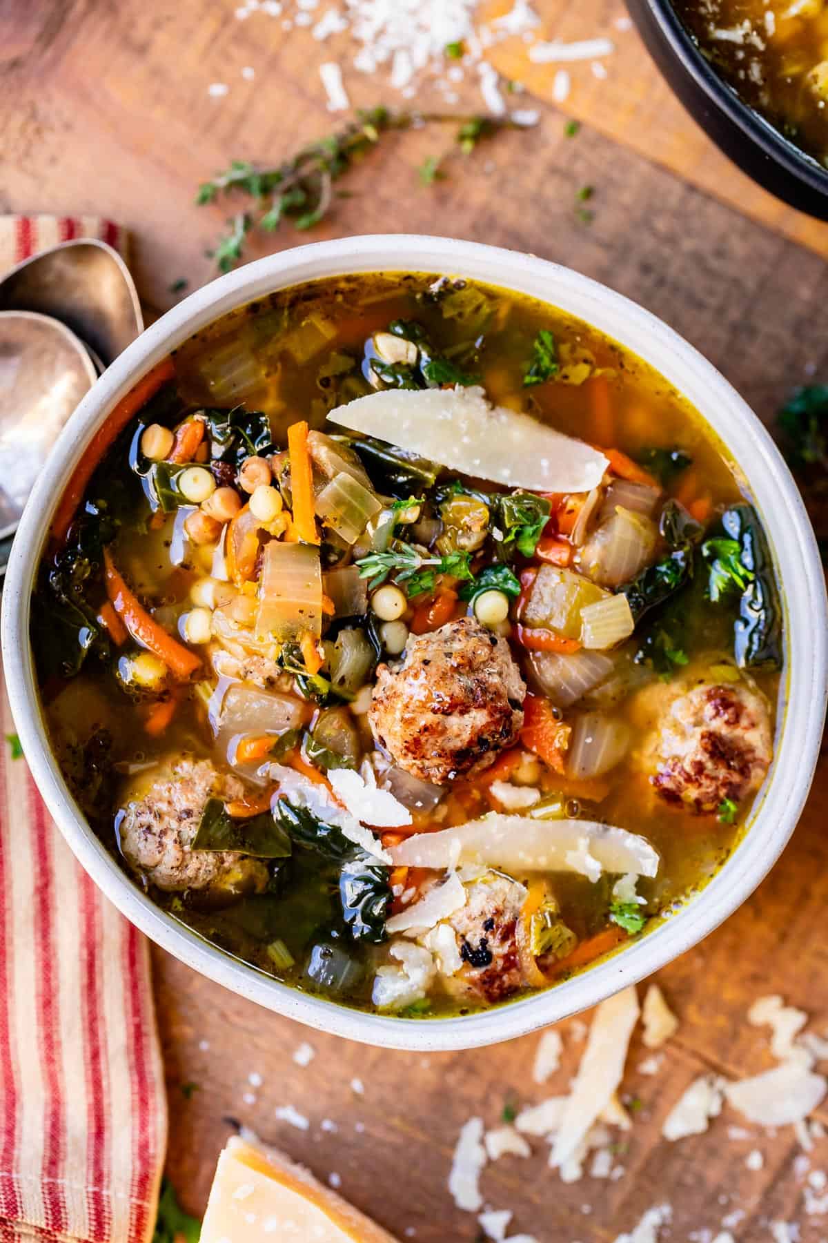 Italian Wedding Soup made of broth, meatballs, greens, and pasta in a white bowl on a cutting board.