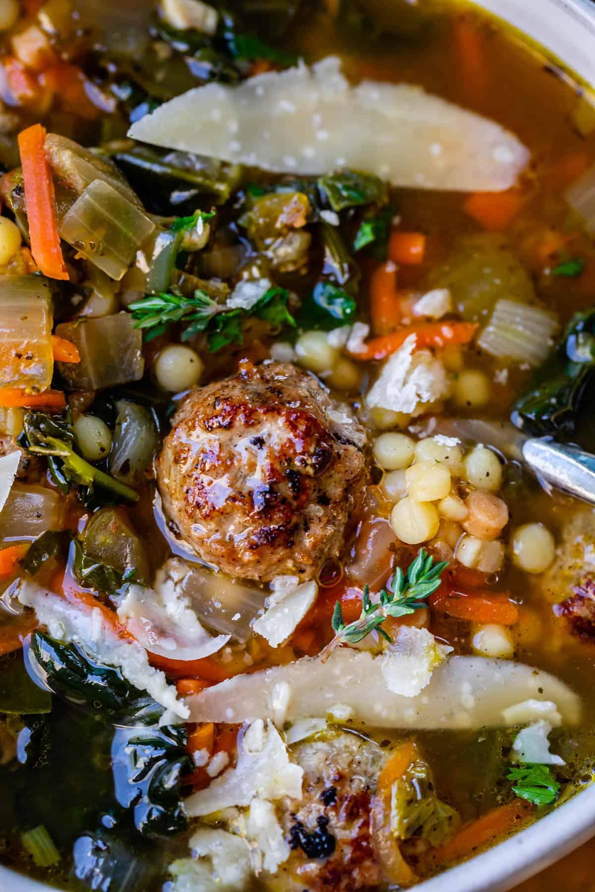 close up of Italian Wedding Soup with meatball, shaved parmesan, pasta, and greens in broth.