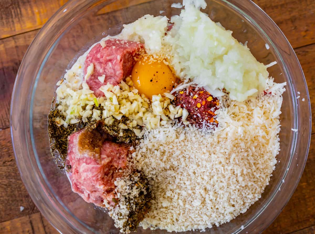 glass bowl with meatball ingredients like ground meat, egg, and bread crumbs.