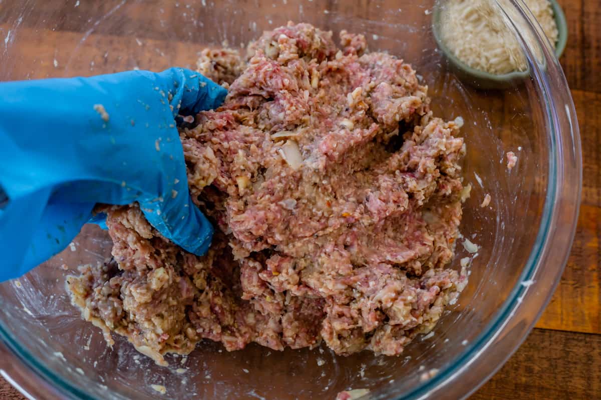 glass bowl with ingredients for meatballs being mixed with a a gloved hand.