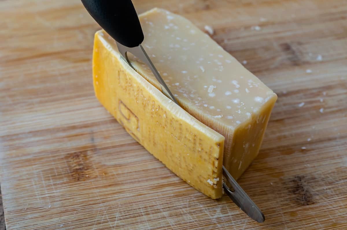 close up of cutting the rind off a wedge of Parmesan cheese.