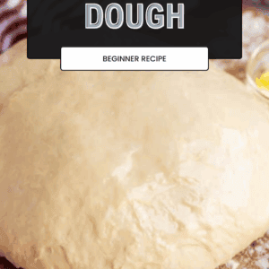 Ball of pizza dough on a floured surface with a striped towel and small bowl of oil in the background. Overlaid text reads, How to Make Pizza Dough – Beginner Recipe using this easy pizza dough recipe.