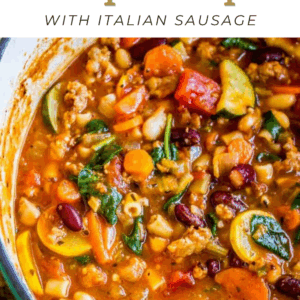 A pot of hearty minestrone soup with Italian sausage, kidney beans, pasta, zucchini, tomatoes, spinach, and carrots in a rich broth. Text above reads, Slow Cooker Minestrone Soup with Italian Sausage.