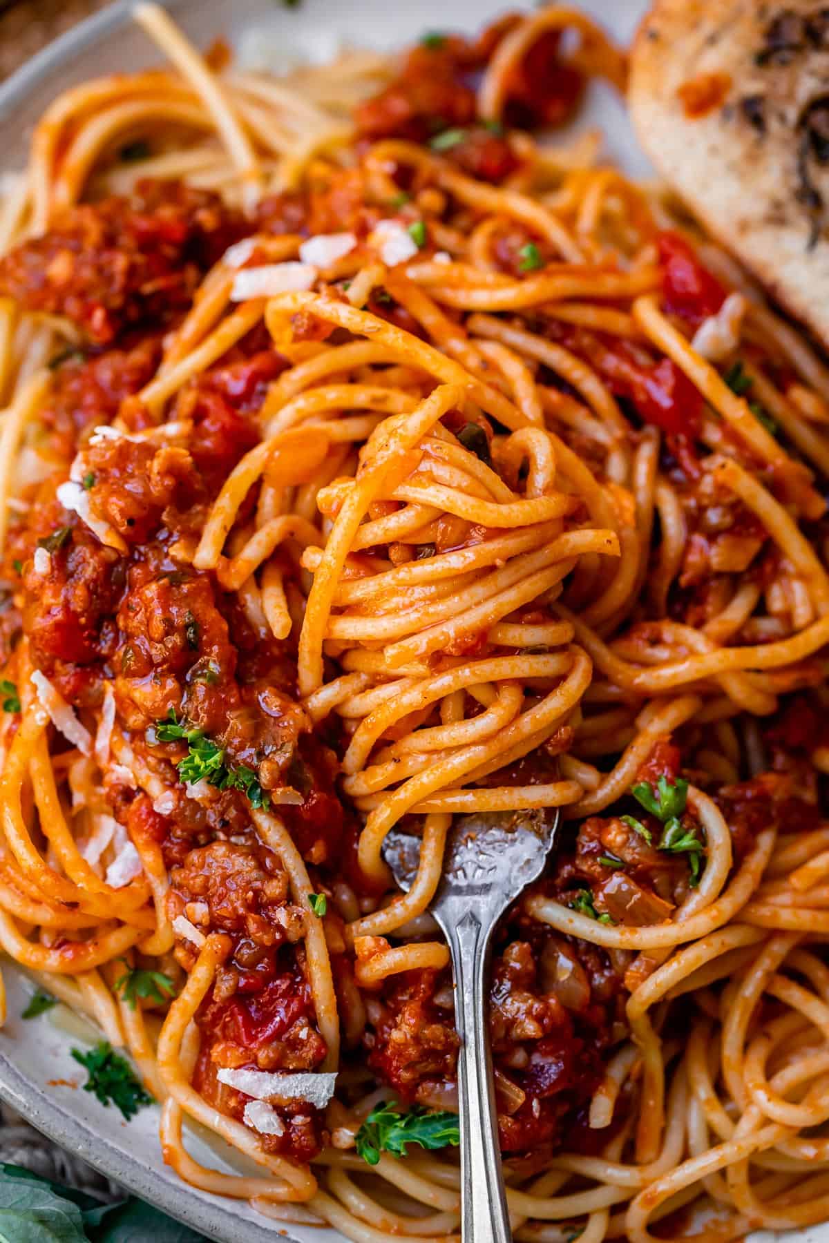 spaghetti noodles covered in spaghetti sauce recipe wrapped around a fork, sitting on plate of spaghetti.