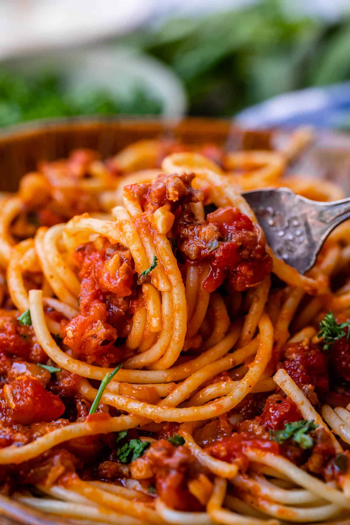 Close up of spaghetti noodles covered in spaghetti meat sauce, wrapped around a fork.