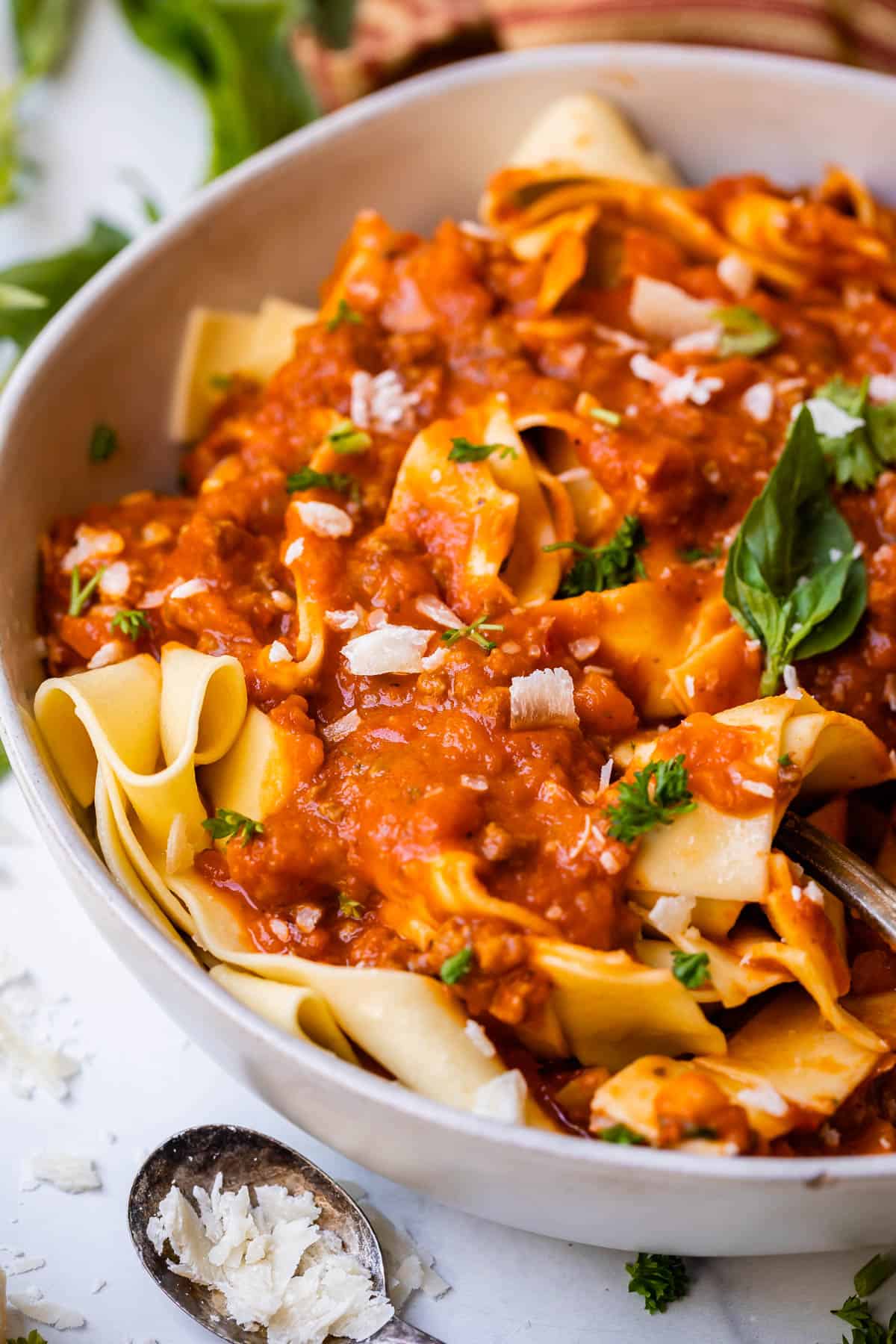 close up of bowl with rich bolognese sauce and noodles with parmesan and basil garnish.