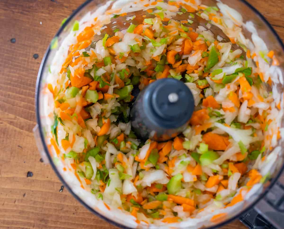 close up of food processor showing chopped onion, celery and carrot.