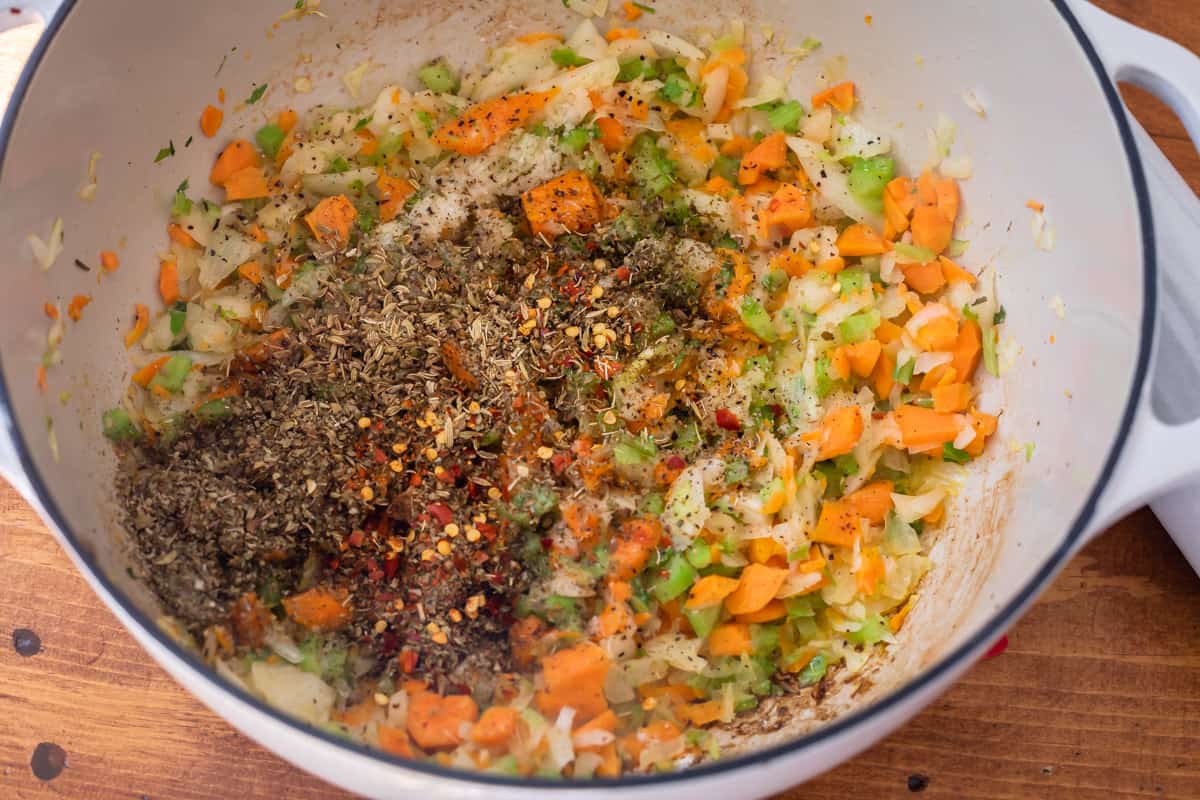 adding seasonings to stockpot with sauteed carrots, celery, and onion.