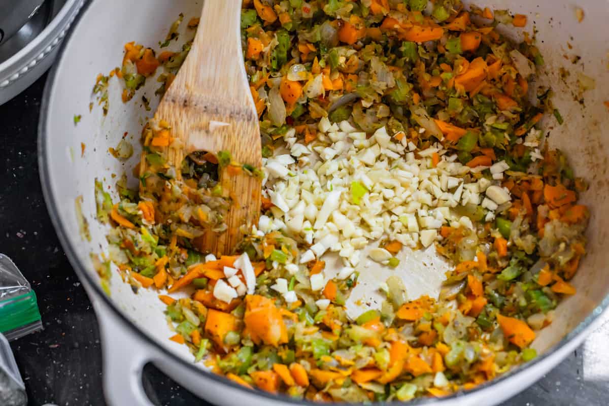 Adding garlic into the stockpot with the sauteed carrots, onions, and garlic.