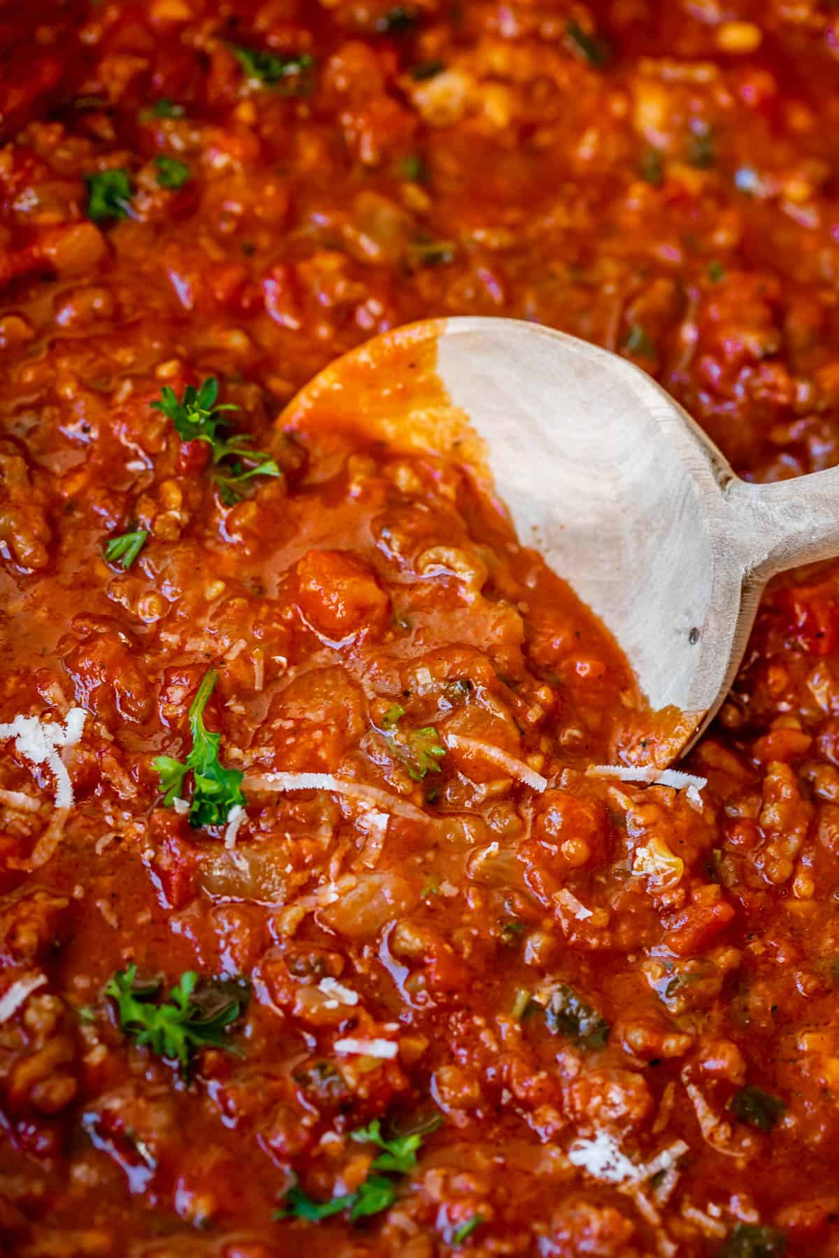 close up of velvety homemade spaghetti sauce with bits of onion, sausage, parmesan, and basil.