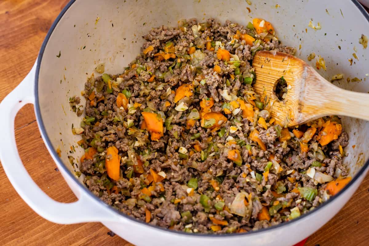 white stockpot with sauteed carrot, onion, celery, garlic, and browned italian sausage.