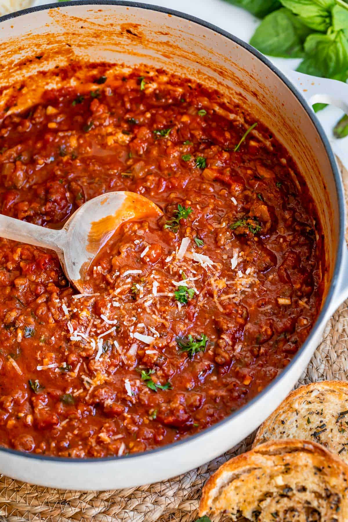 white ceramic cooking pot filled with spaghetti sauce recipe being stirred by a wooden spoon.