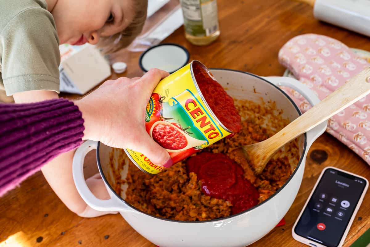 Pouring canned, crushed tomatoes into a stockpot over the seasoned sausage and veggies.