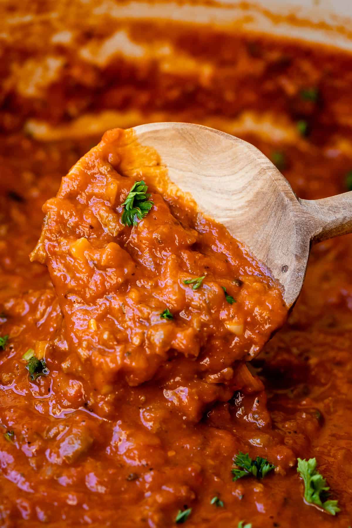 close up of wooden spoon holding deliciously thick and creamy easy bolognese sauce.