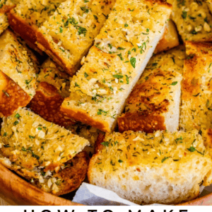 A basket filled with slices of golden, herb-topped garlic bread, garnished with fresh herbs, is shown above text that reads “Classic Garlic Bread - The Food Charlatan.”.