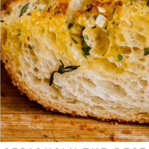 Close-up of golden, crusty garlic bread sprinkled with chopped parsley. Text below reads, Seriously the most irresistible garlic bread of your life. The Food Charlatan.