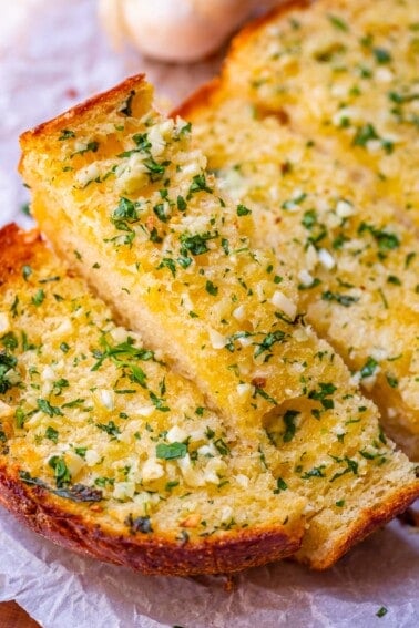 garlic bread recipe with parsley and fresh garlic on white parchment paper.