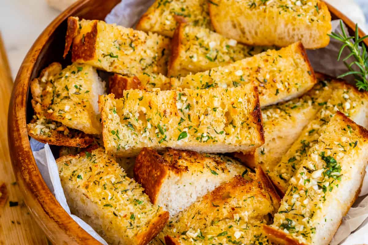 horizontal photo of crispy edge easy garlic bread with parsley in a wooden bowl.