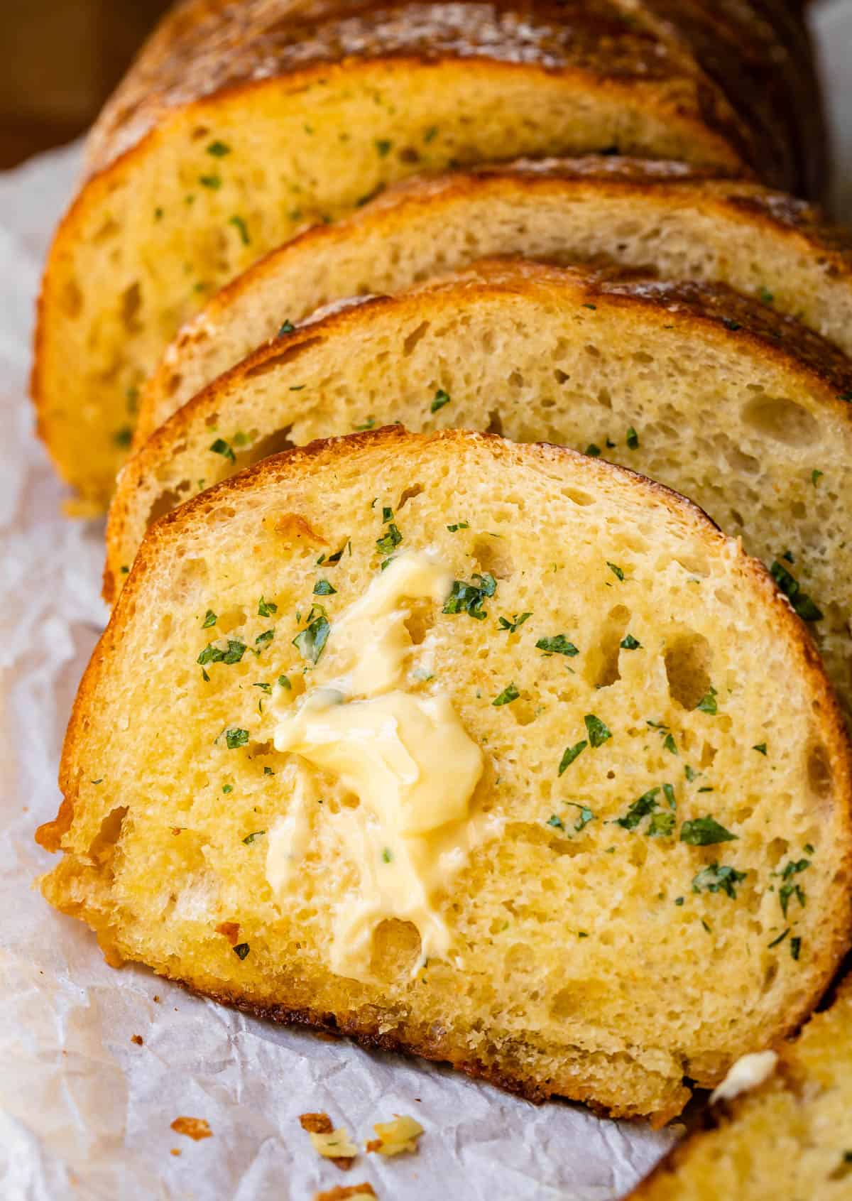 several slices of baked garlic bread with melty butter, garlic, and parsley.