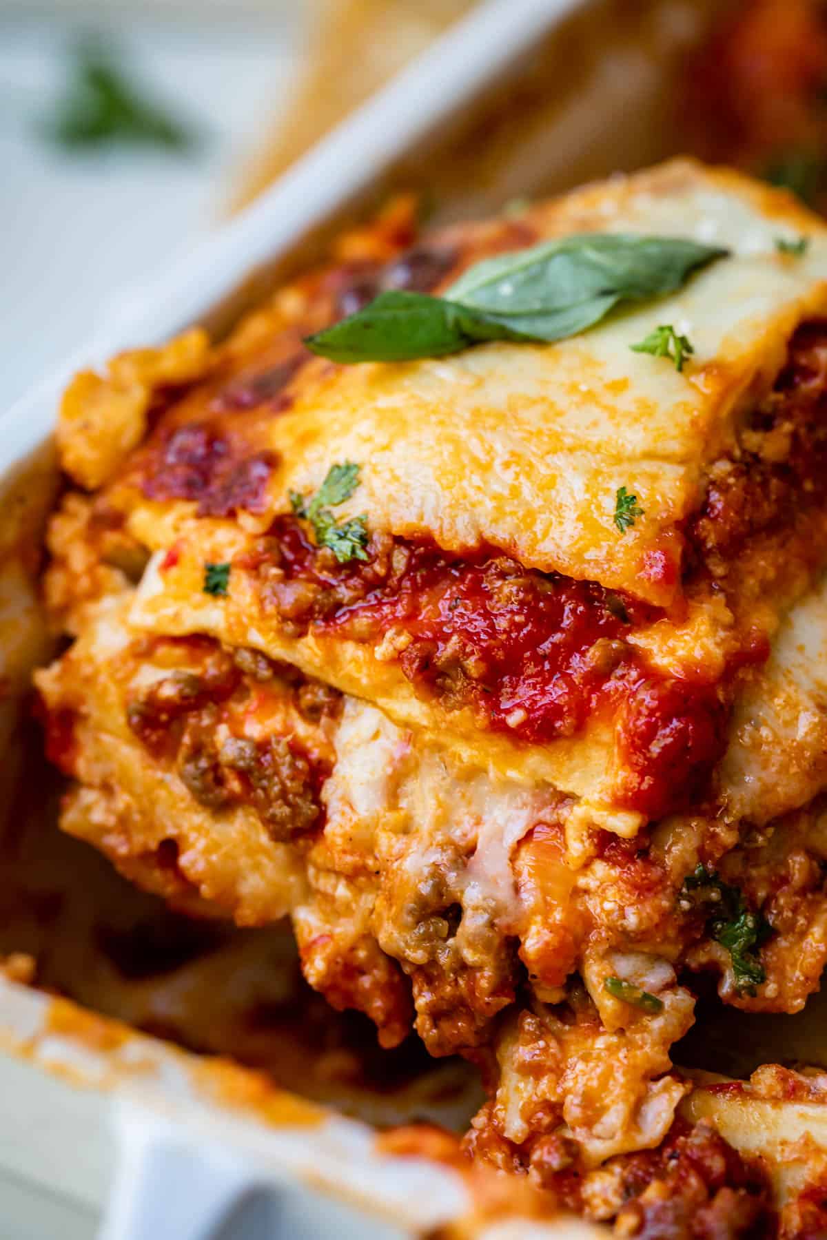 a piece of the best homemade lasagna being lifted from the white pan.